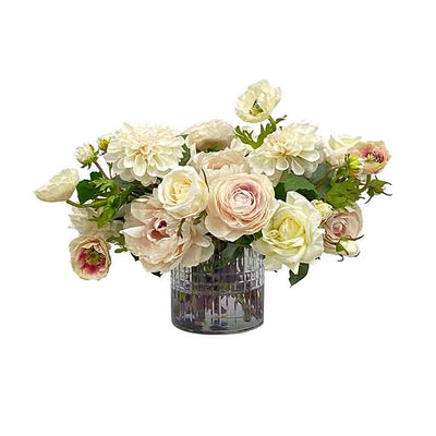 A natural looking cream colored faux rose and ranunculus tabletop arrangement in clear cut glass vase