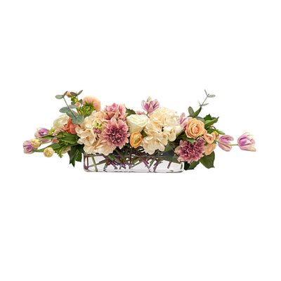 Luxurious faux floral arrangement with Rose Buds, Tulips, and Hydrangeas in a glass vase, placed against background